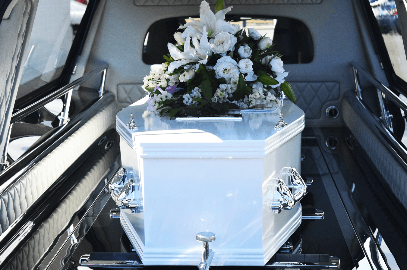 White casket in hearse with large bouquet of white flowers on top